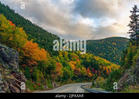 A two-lane highway winds through colorful autumn foliage at Crawford's Notch in New Hampshire's White Mountains. Stock Photo