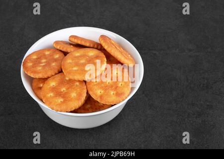 Round salted snack cracker in bowl on black stone surface Stock Photo