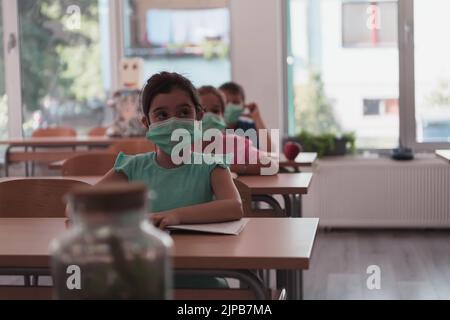 Multiracial group of kids wearing face masks working at class, writing and listening explanations of teacher in classroom Stock Photo