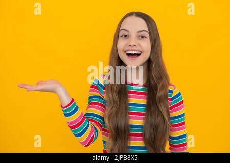 Look at advert. Teenager child points aside shows blank copy space for text promo idea presentation, poses against yellow background. Stock Photo