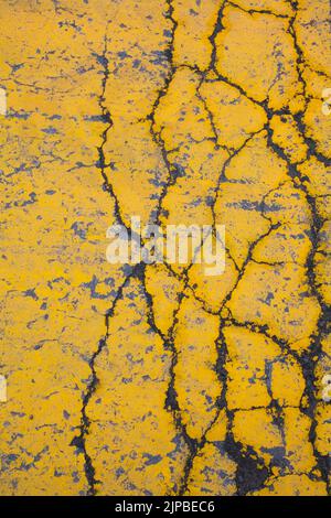 Close-up of cracks on yellow painted asphalt surface in a parking lot. Stock Photo