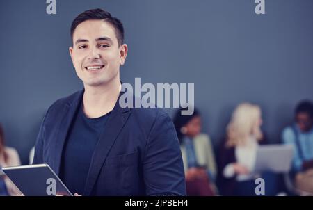 Ive got the confidence to lead. Cropped portrait of a handsome young businessman using a tablet with his colleagues in the background. Stock Photo