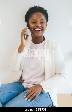 Beautiful African woman standing on the windowsill of a bar talking on the phone with her friends, enjoying her break from work. Stock Photo