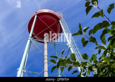 Upward view of a red and white round shaped water tower that resembles a fishing bobber, with blue sky background Stock Photo