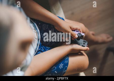 Top view of a boy sitting on the couch and holding two toy cars in his hands. Beautiful portrait. Carefree childhood. Stock Photo