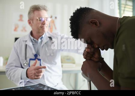 Depressed young African American soldier with walking stick suffering from PTSD visiting psychotherapist Stock Photo