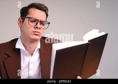 Man with brown suit and glasses elegantly dressed. Business man reading a black book on a white background. Elegant man on white background reading. Confused man reading. High quality photo Stock Photo