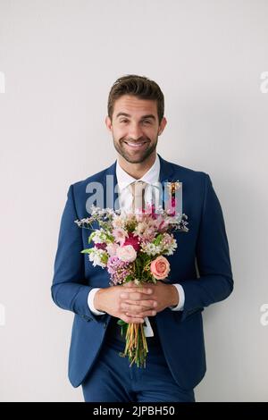 Theyre beautiful but not as beautiful as my bride. Studio shot of a handsome young groom holding a bunch of flowers a gray background. Stock Photo