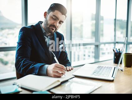 Making his daily work tasks manageable. a young businessman writing in a notebook at his desk in a modern office. Stock Photo