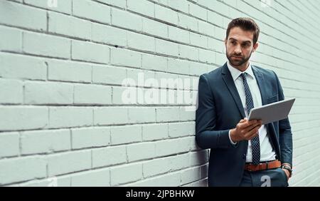 Getting all his updates on the move. a handsome young businessman using a digital tablet outdoors. Stock Photo