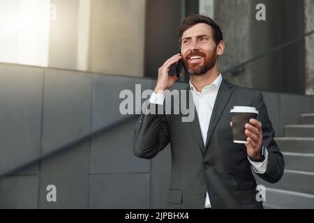 Smiling office worker in suit standing on stairs and drinking coffee during break near office  Stock Photo