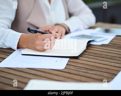 Taking extensive notes. an unrecognizable young businesswoman taking notes while sitting in her office. Stock Photo