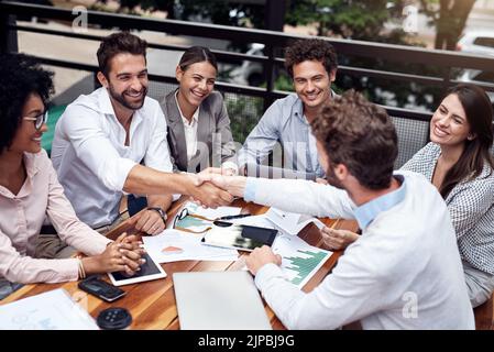 Welcome to the team. two handsome young businessmen shaking hands while sitting with their colleagues outdoors. Stock Photo