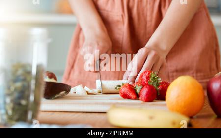 Healthy woman cutting fruit to make a smoothie with nutrition for an organic diet at home. Closeup of caucasian female hands chopping fresh produce Stock Photo