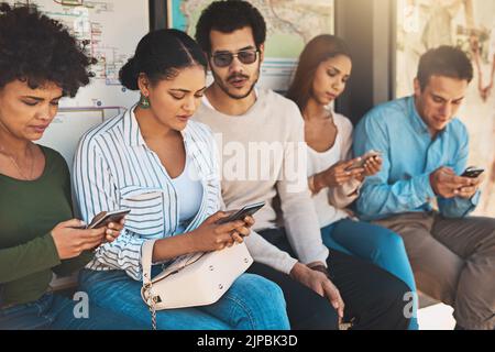We are being very social on our phones today. a group of focused young friends seated next to each other while texting and browsing on their Stock Photo