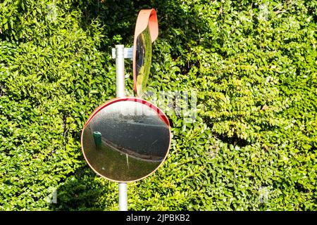 round outdoor convex mirror or driveway mirror or high visibility traffic mirror mounted on a pole on a road or street for blind spot coverage Stock Photo