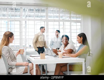 Happy, smiling and friendly colleagues talking on their coffee break or meeting about the news and gossip. Young, global and diverse female employees Stock Photo