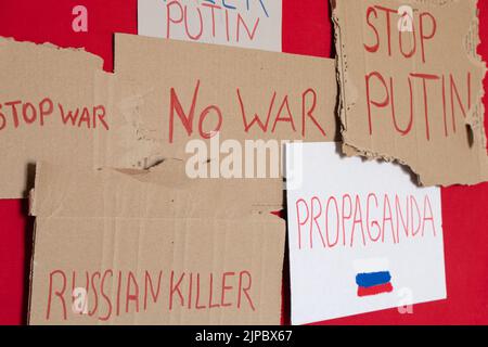 Paper signs with slogans stop war, Russian killer, propaganda, killer Putin, stop Putin, no war on a red background, protest action 2022 Stock Photo