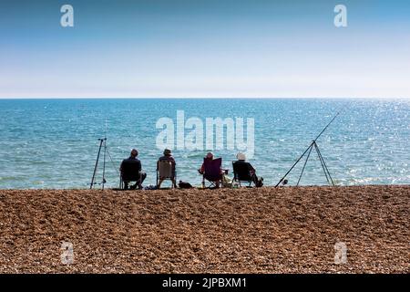 Four fishermen sitting in a shingle beach by a blue sea in silhouette Stock Photo