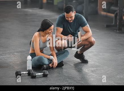 Personal trainer, coach or fitness instructor helping an active and fit woman in the gym. Young female athlete sitting down and managing her workout Stock Photo