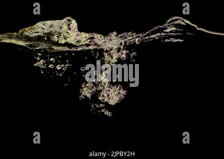 Clear water surface with ripple and bubbles in yellow and purple light on a black nature background Stock Photo