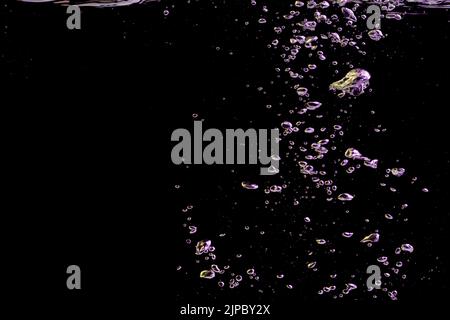 A bubble splash in transparent clear water liquid in yellow and purple light on a black nature background Stock Photo