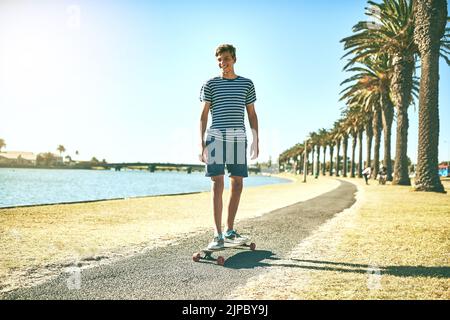 He loves being in the sun. Full length shot of a young boy skating on a pathway alongside a lagoon. Stock Photo