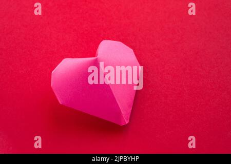 Pink paper heart origami isolated on a blank red background. Valentines day card Stock Photo