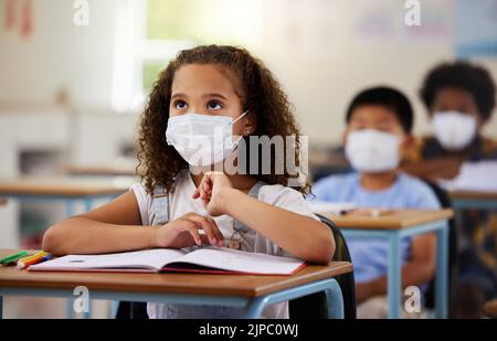 School student with covid learning in class, wearing mask to protect from virus and looking concentrated on education in classroom. Little girl Stock Photo