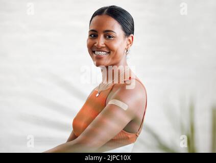 Plaster, vaccinated and covid treatment on a womans arm as shes smiling, happy and proud to stay safe. Healthy female with a band aid protecting Stock Photo