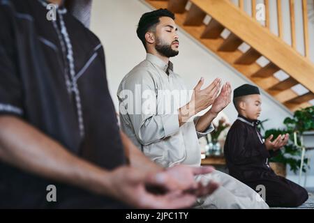 Muslim family praying together at home with eyes closed during fajr, dhuhr, asr, maghrib or Isha. Practicing religion and cultural tradition to serve Stock Photo