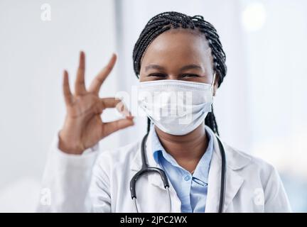 Doctor gesturing okay hand sign, symbol and emoji to express success and agreement in a good clinic or hospital. Portrait of a smiling medical Stock Photo