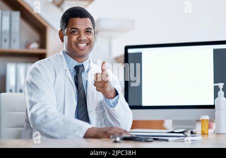 Doctor, medical practitioner and healthcare worker showing thumbs up for FDA or drug approval in a hospital with blank screen copy space on a computer Stock Photo