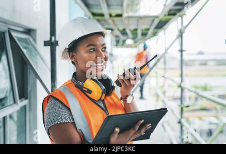 Construction worker with tablet, walkie talkie or radio talking, instructing and checking building progress on development site. Architect manager Stock Photo