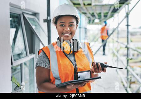 Portrait of proud black construction worker leading with power while managing site logistics on tablet. Happy female engineer supervising a building Stock Photo