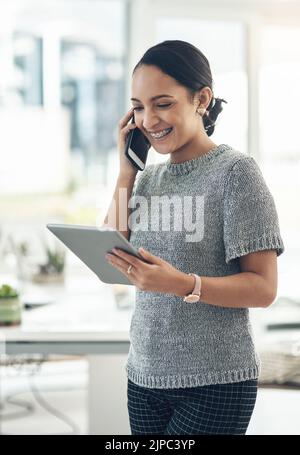 Professional smiling businesswoman talking on phone call with client in modern office. Young design employee working on appointment booking on tablet Stock Photo