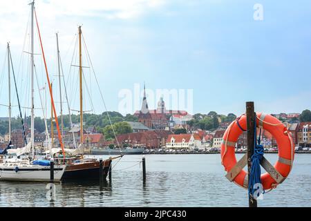 Flensburg, Germany, July 25, 2022:  Yacht harbor with sailing ships and lifebuoy ring, old town with St. Marien curch on the other shore of the fjord, Stock Photo