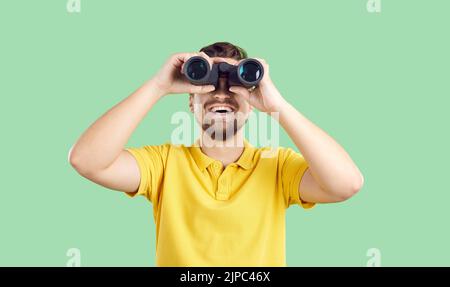 Happy young traveller isolated on green background looking through binoculars and smiling Stock Photo