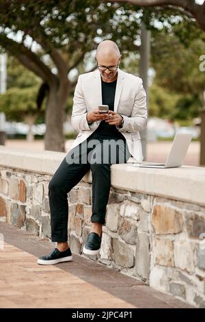 Stylish, cool smiling businessman on a phone in the park outside in nature. Happy man texting, chatting or reading social media messages on a Stock Photo