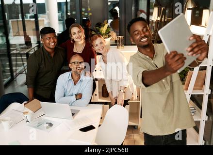 Excited, happy and smiling team of corporate workers taking fun selfie on a tablet in office. Fun, playful and cheerful marketing team posing for Stock Photo
