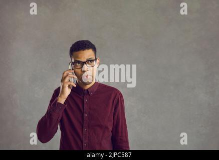 Confused young black man holding mobile phone, making call and waiting for answer Stock Photo