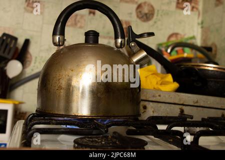 An old dirty kettle stands on a gas stove in the morning in the kitchen at home, a kettle on the stove, gas stove, gas price 2022 Stock Photo