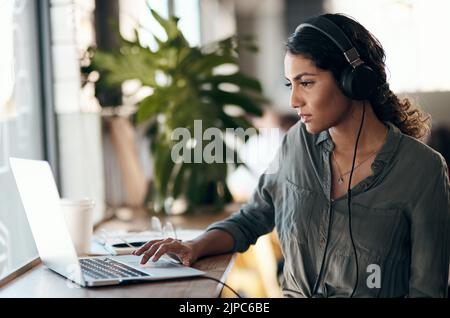 Female student working on laptop with headphones for a university project in a cafe, restaurant or coffee shop. Thinking and studying young university Stock Photo