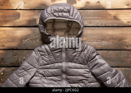 Gray women's warm winter jacket lies on a wooden table, fashionable outerwear Stock Photo