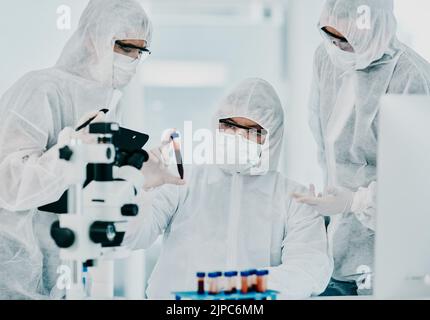 Hazmat suit scientists with test tube in medical research, healthcare or science cure testing for covid, marburg virus or ebola. Group of laboratory Stock Photo