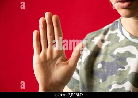 Hand of a girl in a camouflage uniform on an isolated red background close-up, hand gesture, Stock Photo