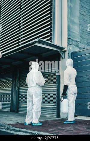 Medical team and covid hygiene healthcare workers wearing hazmat suits for safety while at quarantine site outside. In protective gear for cleaning Stock Photo