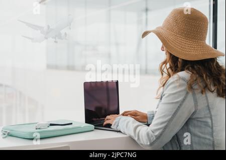 Woman using laptop at table near window in airport window Stock Photo