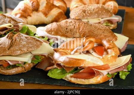 High angle of assorted appetizing sandwiches with ham cheese and veggies served on slate boards on wooden table in restaurant Stock Photo