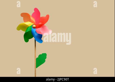 Toy windmill with colorful petals green leaf and wooden stick against beige background Stock Photo